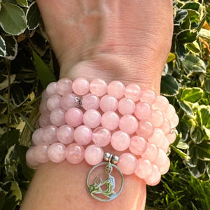 Gros plan sur un mala en quartz rose naturel aux nuances délicates avec pendentif Bouddha assis.
Mala quartz rose 108 perles porté au poignet avec pendentif Bouddha symbolisant la sérénité et la méditation.