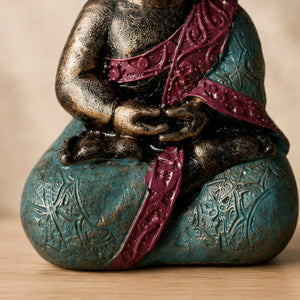 Gros plan sur les mains en méditation et les motifs colorés de la statuette Bébé Bouddha en polyrésine