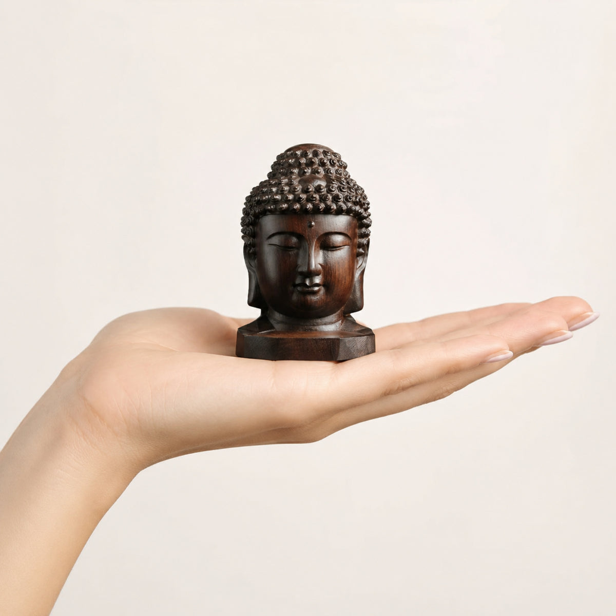 Petite Tête de Bouddha en bois d’acajou de 6 cm présentée dans la main pour montrer son format